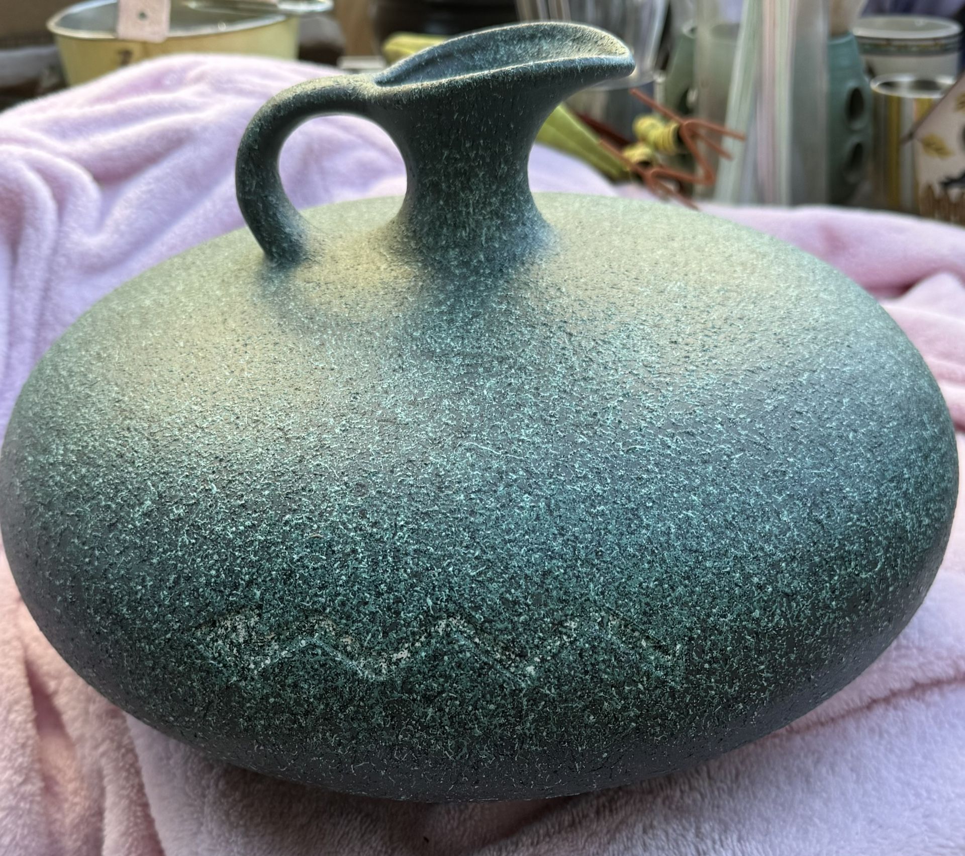 large, round, green pottery vase with a textured surface and a small spout. It Has a incised zigzag patter Of A Snake