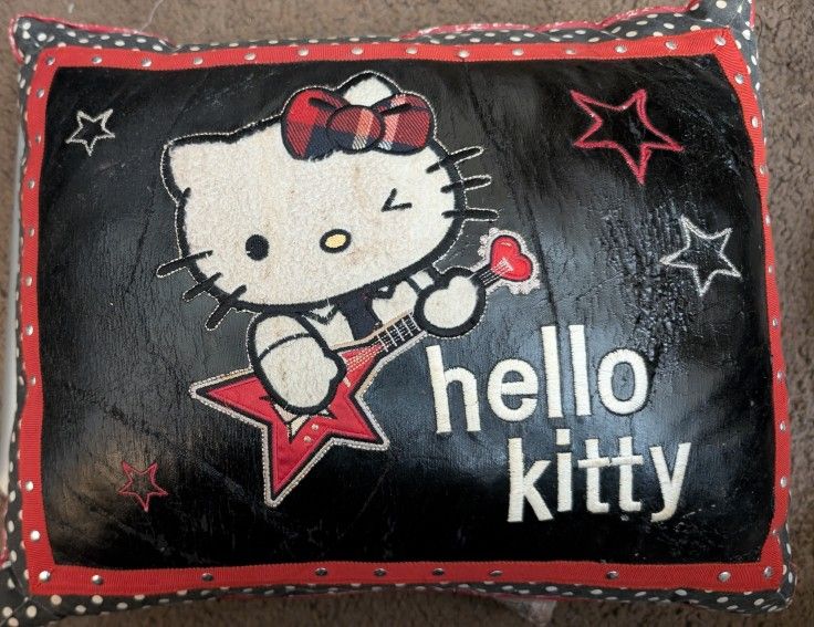 Hello Kitty Pillow. Black Pleather Which Is Wearing, Wrinkling As A Small Hole Starting To The Right Of The Red Embroidered Star. Shiney Rivets Around