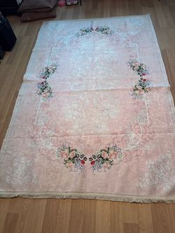 Floral pattern area rug with a soft pink background. Fringed edges on both sides. Fabric construction. 8 by 5