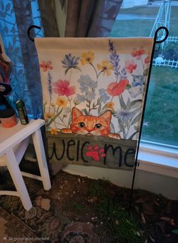 Cute garden flag has an orange cat peeking over a wooden 'WELCOME