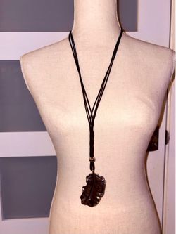 The necklace features a leaf-shaped pendant with a dark metallic finish suspended from a black cord.