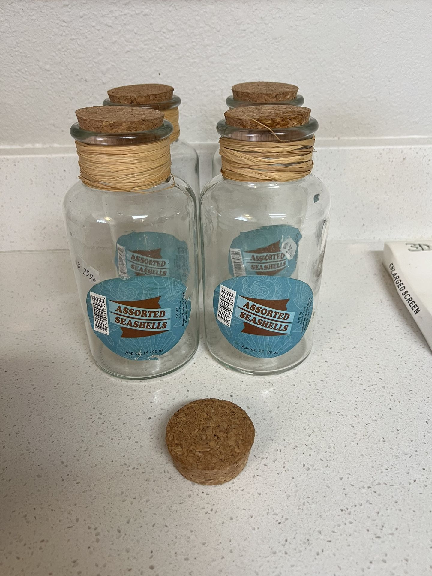 glass bottle with a cork stopper containing a label for assorted seashells. The product is labeled as "Assorted Seashells". The container is an empty