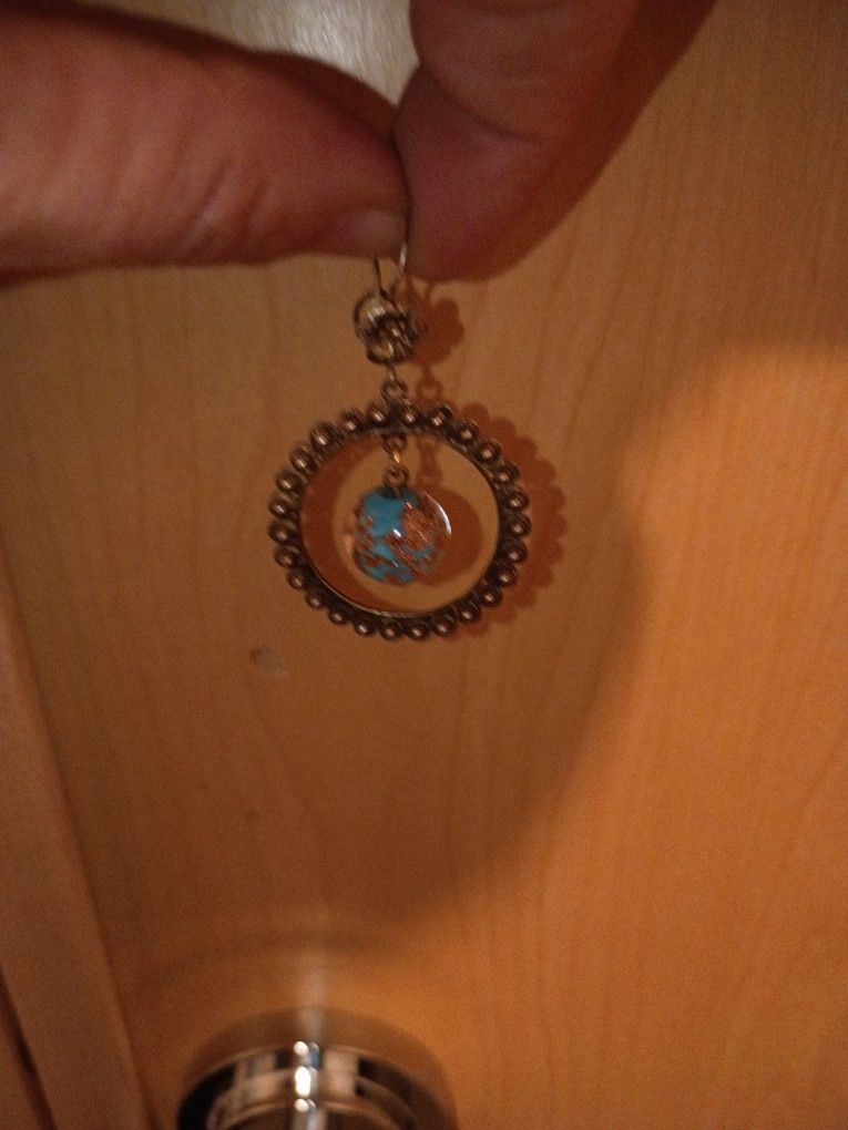 This is a pair of gold-toned dangle earrings featuring a central turquoise-colored bead within a circular, beaded frame.