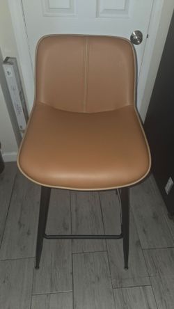 Modern bar stools feature camel brown synthetic leather upholstery with a central vertical seam. The set includes two stools with black tapered metal 