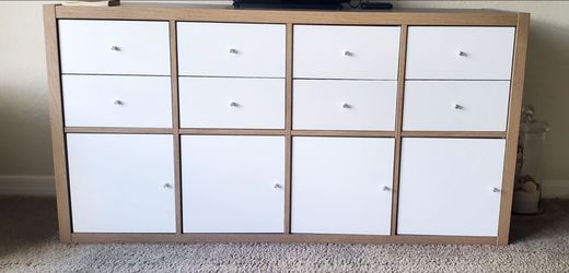 IKEA Kallax shelving unit in oak-effect finish with white door and drawer inserts. 58" Long x 15 1/2" Wide x 30" High.