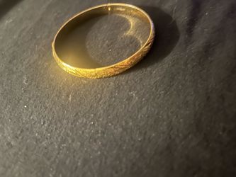Elegant gold-toned bangle bracelet iwith an intricate etched floral and geometric pattern. This piece is a rigid circular design with a polished inter