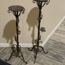 Set of two ornate metal candle or small plant holder stands with leaf and vine design.