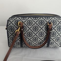 Tory  eatures a woven canvas body in navy and cream with an all-over repeating circular geometric logo pattern arranged in a diamond grid.