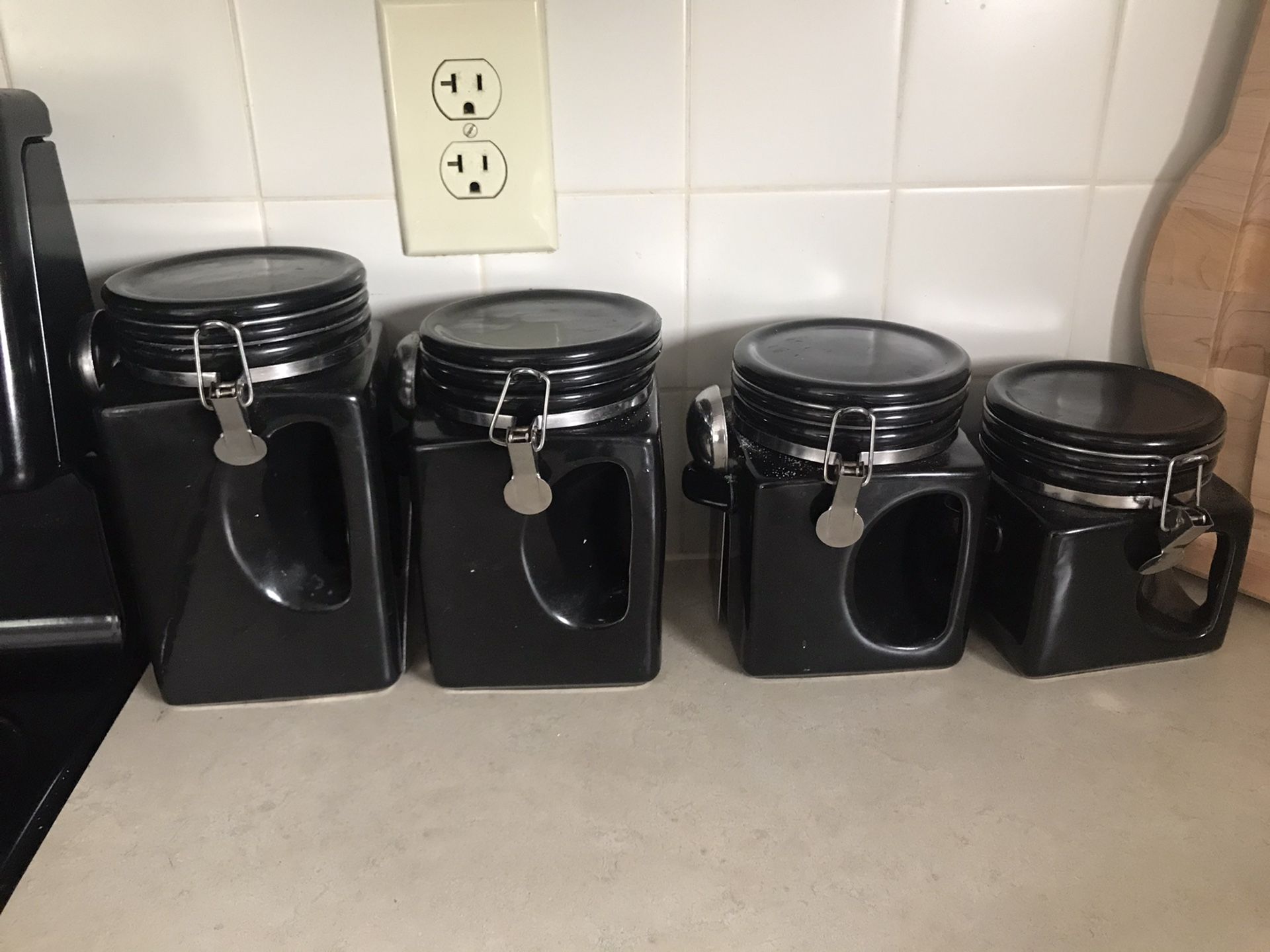 Four black kitchen storage containers with spoons