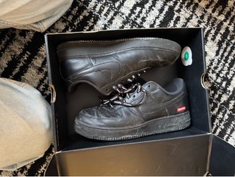 black leather Nike Air Force 1 Low sneakers from the 2020 collaboration with Supreme, featuring distinctive branding on the laces.