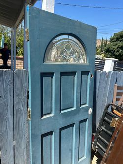 Solid wood exterior door has a blue painted exterior and a white painted interior. It features a decorative arched glass insert with leaded-style deta