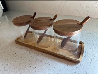 Set Of 3 Clear Glass Spice Cellars Featuring Acacia Wood Lids, Wooden Spoons, And A Matching Woods