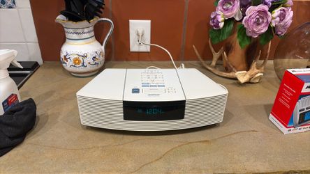 white Bose Wave Radio/CD player features a sleek, compact design with a top-loading CD slot and a prominent digital display$100