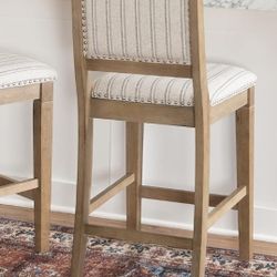 Linon Emmy or Stella grey wash wood counter stool with a striped fabric upholstered seat and brushed silver nailheads. 