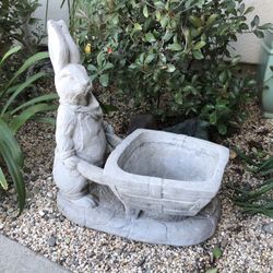 An adorable cement rabbit pushing cart planter 