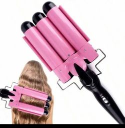 Pink three-barrel hair waver has a black handle and power cord. This styling tool includes temperature settings for 180°C and 210°C. A metal safety st