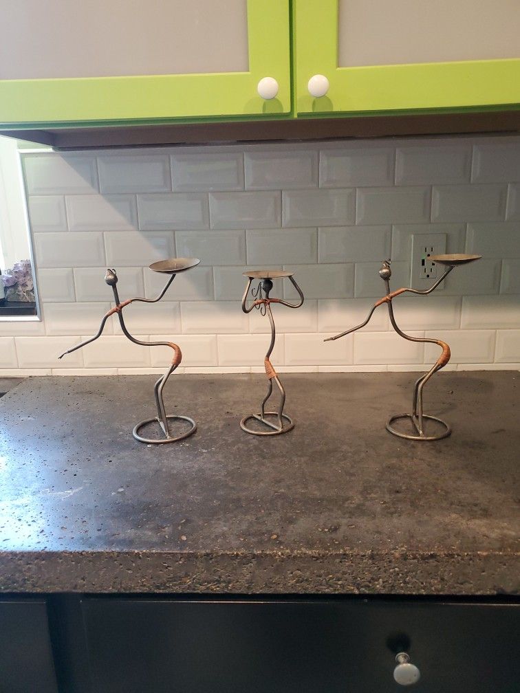 Three candle holder figures made out of metal.