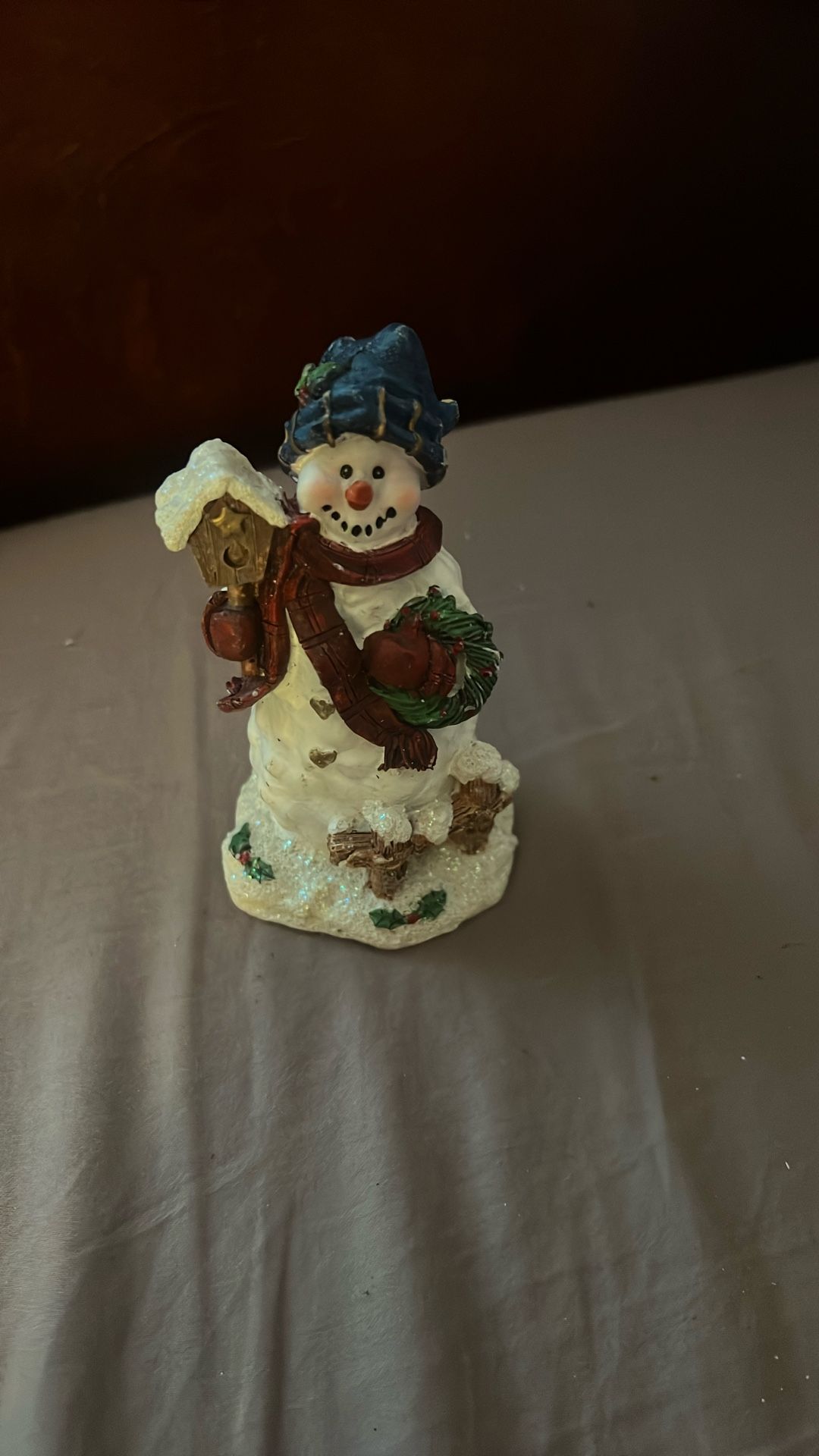 Snowman figurine holding a wreath and a birdhouse