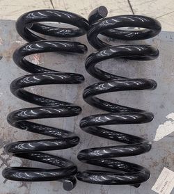 Durable black steel coil springs for vehicle suspension. This pair has a glossy black finish and measures approximately 14 inches in length. The set i