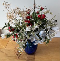 Artificial floral arrangement in blue glass vase, vase is 8”. Tall with glass beads in the bottom.