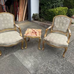two gold and silver chairs with marble topped side table.