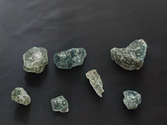 Raw emerald green crystals come in a set of seven unpolished pieces. These natural stones have a translucent light green color with varying shapes.