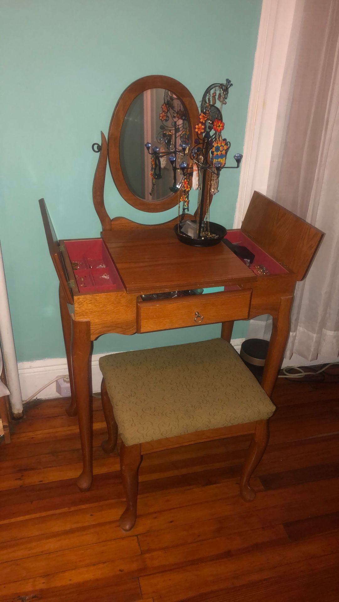 Queen Anne style wooden vanity set with an oval mirror and cushioned stool. 
