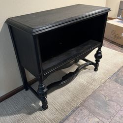 A black painted wooden console table with turned legs and carved accents.