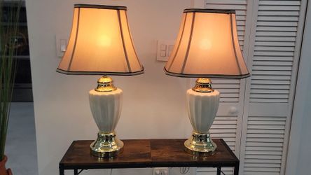 A pair of classic table lamps 25" featuring ribbed ivory ceramic bases, polished gold-tone metal accents, and beige Empire-style fabric shades with da