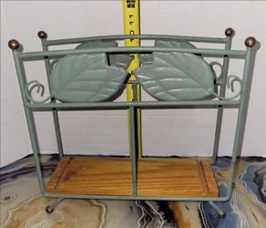 Decorative green metal shelf stand with leaf detail accents and wood bottom shelf. Approx. 10.5” wide x 9” tall.