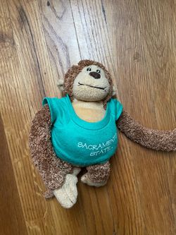 Cute Monkey Plush Toy For sale: a charming monkey plush toy. Design: The monkey wears a vibrant turquoise T-shirt. Appearance: Soft fur, adorable