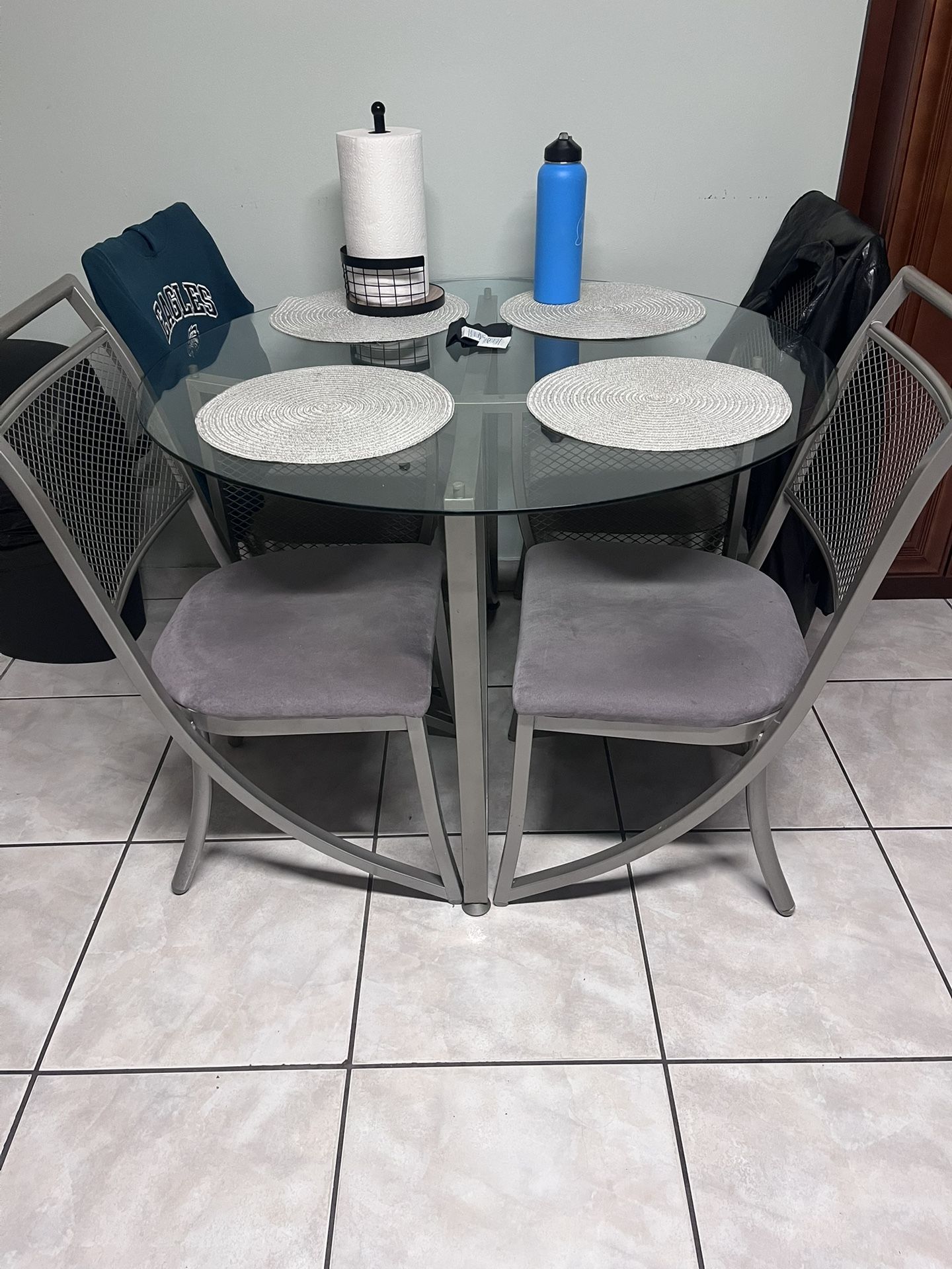 Round glass dining table with metal frame and four cushioned chairs.