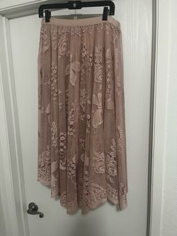 Dusty pink lace midi skirt has an asymmetrical high-low hemline. The fabric features an intricate floral and butterfly pattern with a scalloped edge.