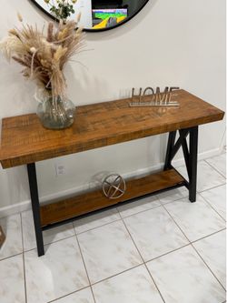 A 47.25-inch wide console table with a wood-look top and a black metal X-base frame, plus a lower open shelf for storage or decor