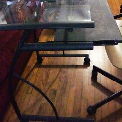 Glass top black metal computer desk and wooden chair on casters