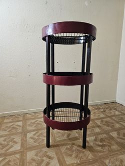 A round, three-tiered shelf made of red and black metal.
