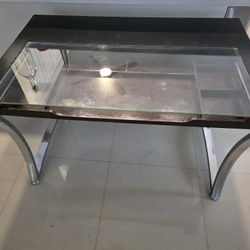 Wooden desk with a glass top and stainless steel legs. It measures 48 inches wide x 31 inches high and deep