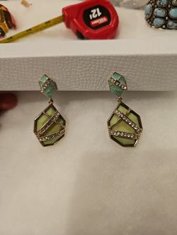 A pair of drop earrings featuring a geometric design with green faceted stones and clear rhinestone accents, set in a gold-toned metal