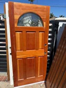 Solid wood front door with a natural finish. This door has a decorative arched glass insert with brass-colored caming and a beveled design. It is a si
