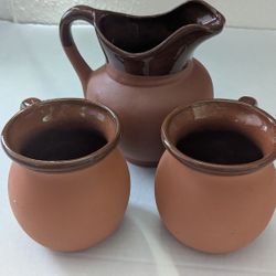 set of vintage pottery, specifically a pitcher and two mugs, crafted from red terracotta