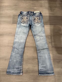 Rock Revival Light blue boot cut jeans with faded, distressed finish. Prominent embroidered R logos on back pockets. Classic mid-rise fit with subtle 