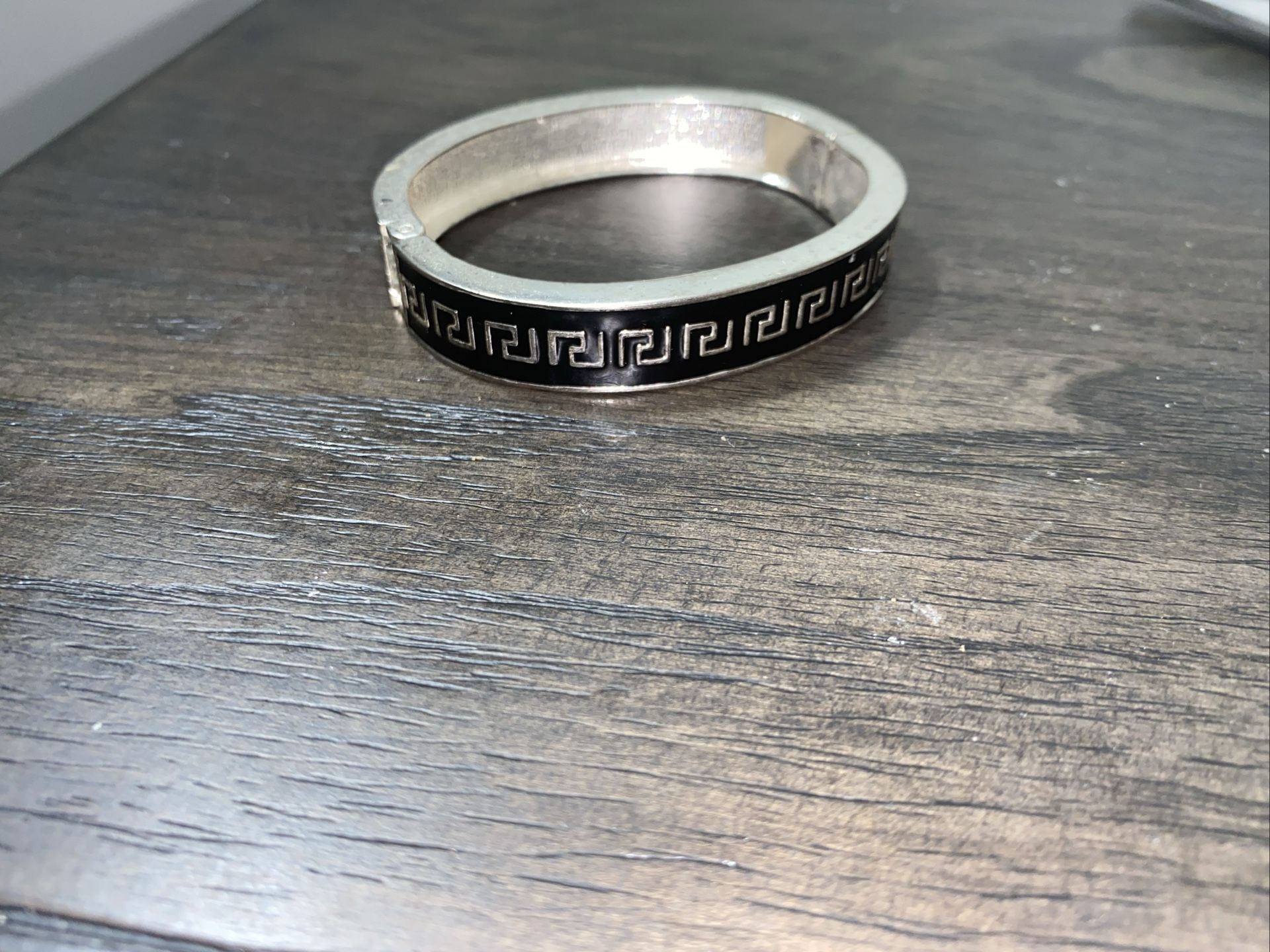 This is a sterling silver hinged bangle bracelet with a black Greek key pattern.