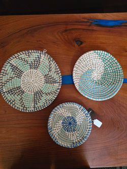 Set of three handwoven straw wall baskets in natural tones with blue and green accent patterns. Lightweight and decorative, they add texture and a coa