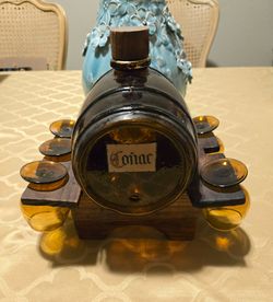 Vintage Mid Century Amber Glass Barrel-style Liquor Decanter and Matching Shot Glass Set labeled "Coñac," resting on a dark wooden stand.
