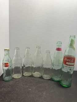 Lot of 7 vintage and collectible glass soda bottles featuring Coca-Cola and Pepsi-Cola. Includes several clear embossed Coke bottles, a Pepsi-Cola 16
