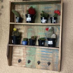 Distressed or rustic-style wooden wall shelf unit with three shelves and four hooks along the bottom