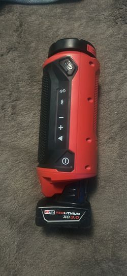 Durable Milwaukee M12 Bluetooth jobsite speaker is red and black with a rugged exterior. It has a built-in handle, side-mounted control buttons, and a
