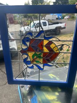 Nice stained glass window in a frame. Probably depicting a coat of arms is my guess. It’s in a nice blue frame with the old  wavy looking clear glass 
