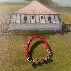 This is a red braided leather bracelet with a gold-toned clasp and bead accents