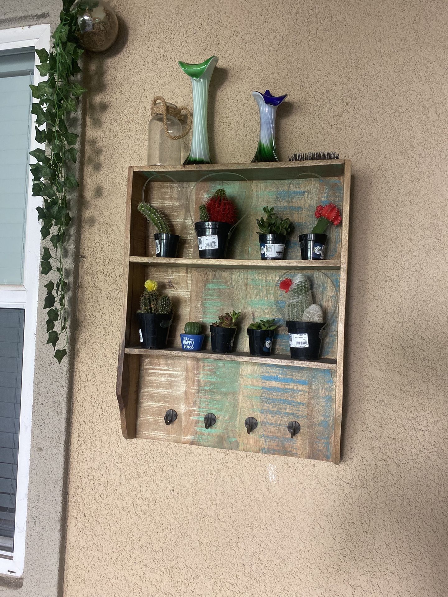 Distressed or rustic-style wooden wall shelf unit with three shelves and four hooks along the bottom
